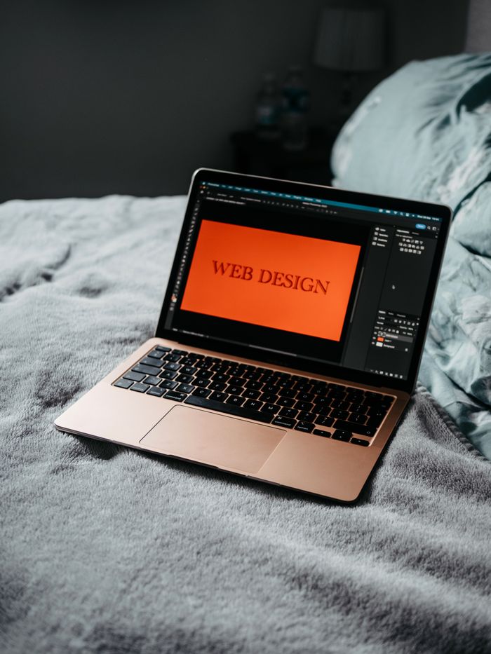 about-us-01 A laptop on a bed showing web design software, creating a cozy workspace.